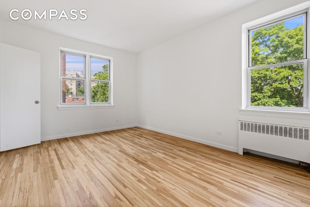 unfurnished room featuring baseboards, light wood finished floors, and radiator heating unit