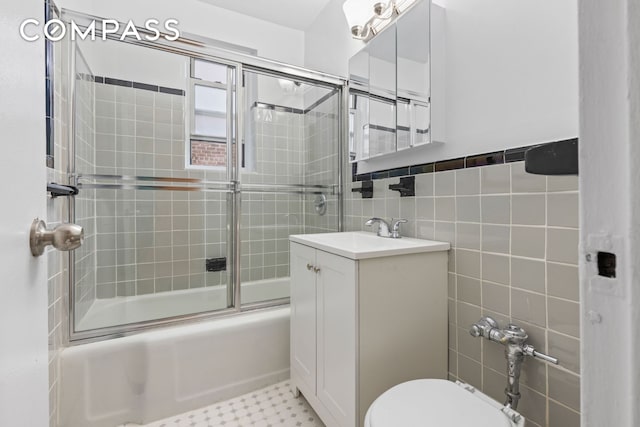 bathroom with toilet, bath / shower combo with glass door, vanity, and tile walls