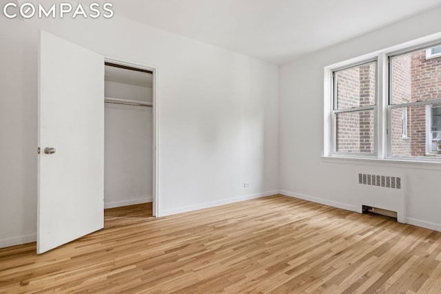 unfurnished bedroom featuring a closet, light hardwood / wood-style floors, and radiator heating unit