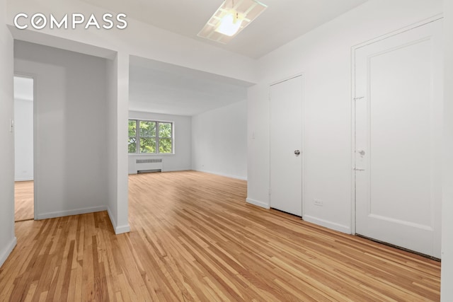 unfurnished room featuring baseboards, light wood finished floors, and radiator heating unit