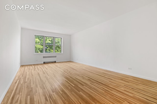 spare room with baseboards, light wood finished floors, and radiator heating unit