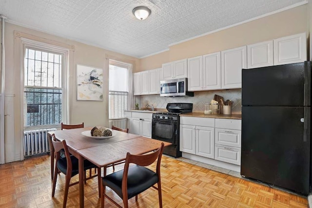 kitchen featuring plenty of natural light, radiator, white cabinets, and black appliances