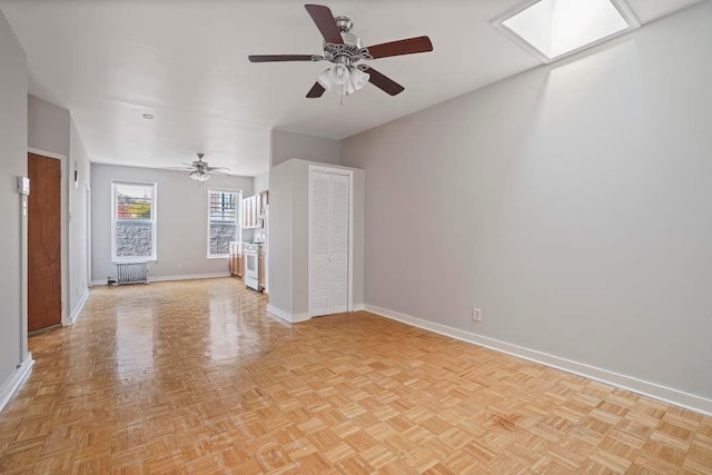 unfurnished living room with a skylight, radiator heating unit, light parquet flooring, and ceiling fan