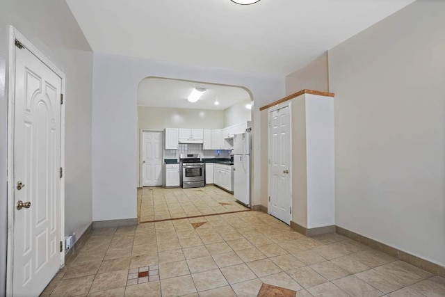 kitchen featuring light tile patterned floors, white cabinetry, white refrigerator, stainless steel range, and decorative backsplash