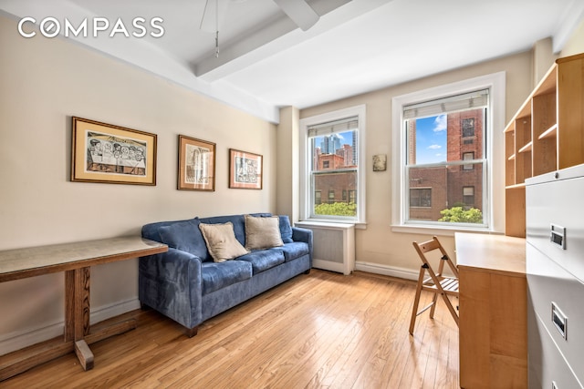 sitting room featuring beam ceiling, light wood-style flooring, radiator heating unit, and baseboards