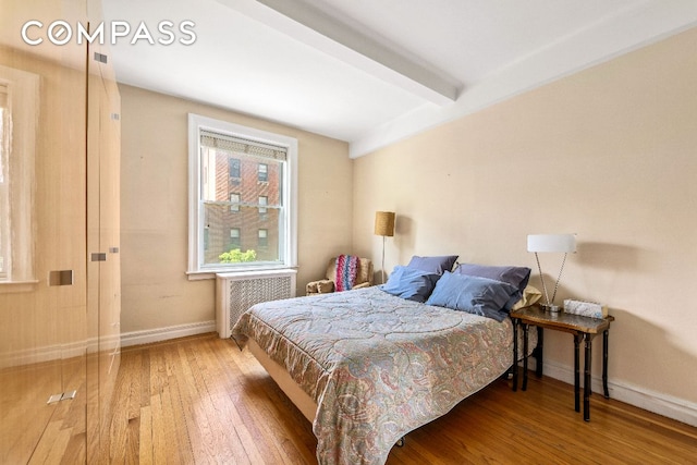 bedroom featuring wood-type flooring, radiator, and beam ceiling