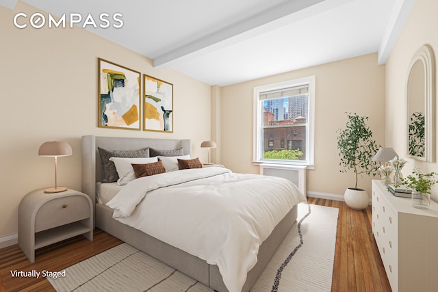 bedroom with beam ceiling, baseboards, and wood finished floors