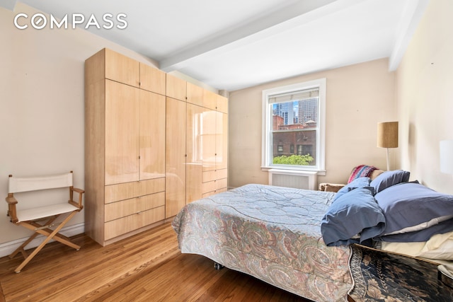 bedroom with beamed ceiling, light wood-style flooring, and radiator heating unit