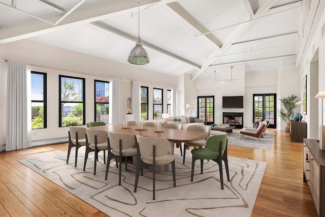 dining room with beamed ceiling, baseboard heating, light wood-type flooring, a fireplace, and high vaulted ceiling