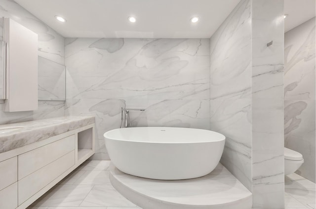 full bathroom featuring marble finish floor, a freestanding bath, stone wall, and vanity