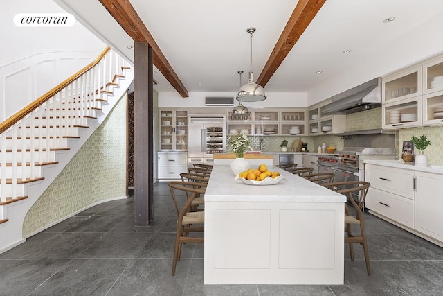 kitchen featuring a breakfast bar, decorative backsplash, a kitchen island, wall chimney range hood, and beamed ceiling