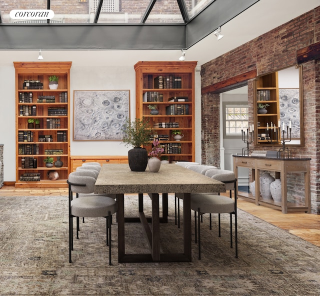 dining space featuring brick wall, wood finished floors, a towering ceiling, and track lighting