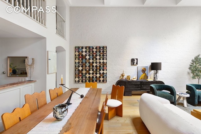 dining area featuring brick wall, a towering ceiling, and light hardwood / wood-style floors