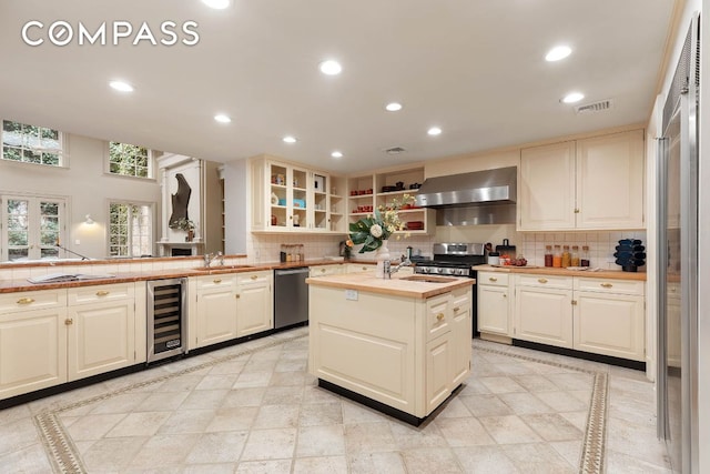 kitchen featuring sink, appliances with stainless steel finishes, wall chimney range hood, beverage cooler, and backsplash