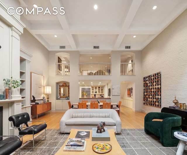 living room featuring coffered ceiling, wood-type flooring, a towering ceiling, and beam ceiling