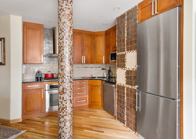 kitchen featuring wall chimney exhaust hood, stainless steel appliances, decorative backsplash, sink, and light hardwood / wood-style flooring