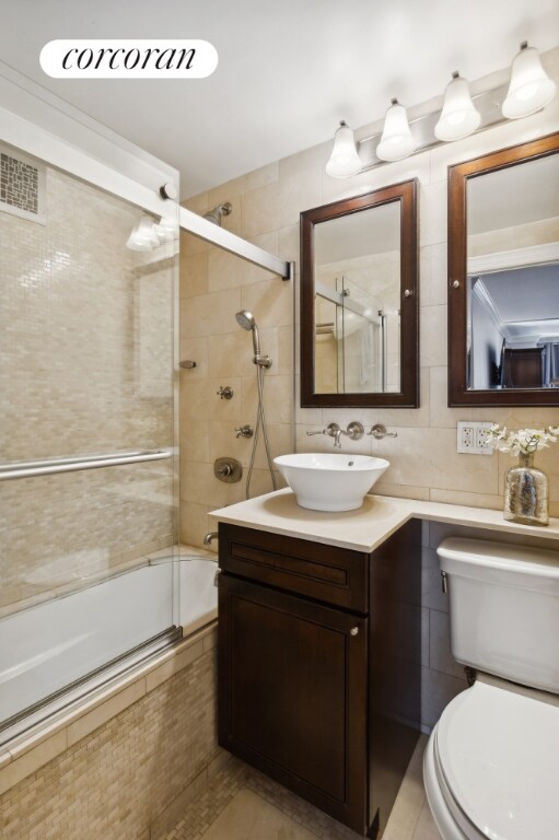 full bathroom featuring tile walls, shower / bath combination with glass door, vanity, and toilet