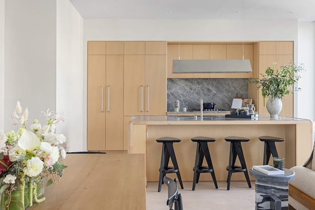 kitchen with a kitchen bar, backsplash, and light brown cabinetry