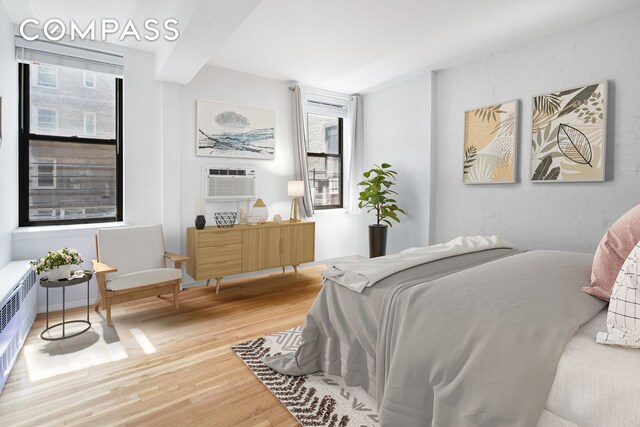 bedroom featuring beam ceiling, radiator, a wall mounted air conditioner, and wood finished floors