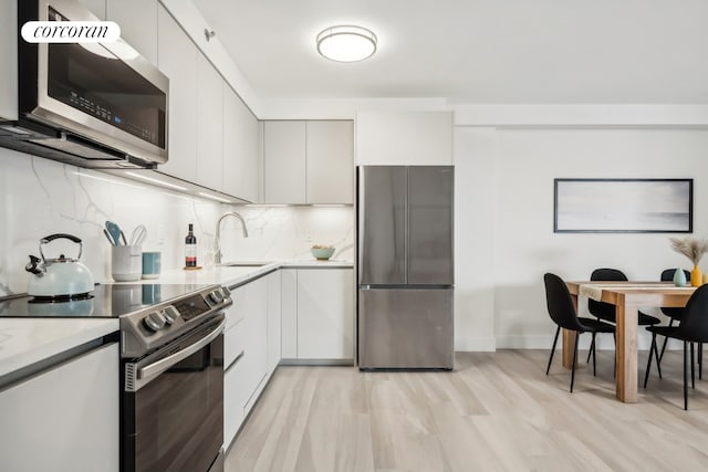 kitchen featuring modern cabinets, a sink, backsplash, white cabinetry, and appliances with stainless steel finishes