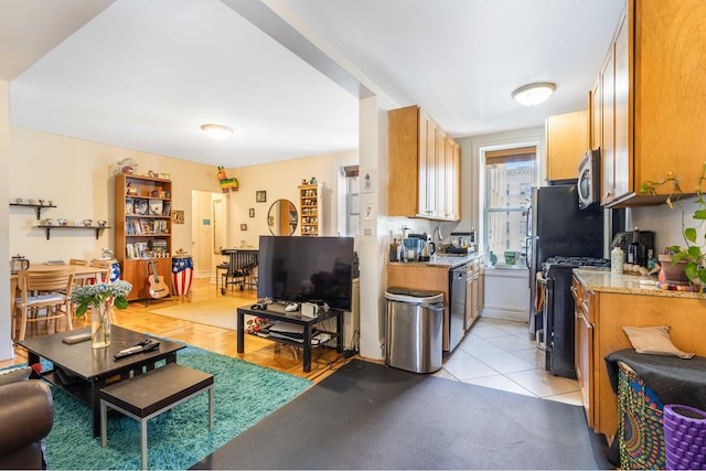 kitchen featuring light tile patterned floors, stainless steel appliances, light stone counters, and brown cabinetry