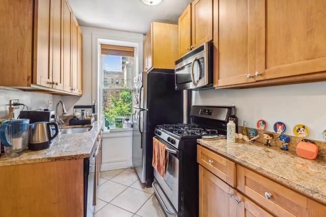 kitchen featuring light stone counters, light tile patterned floors, stainless steel appliances, brown cabinetry, and a sink