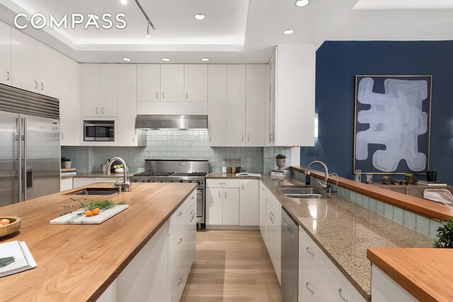 114 Liberty St Unit 7, New York City, NY 10006 - kitchen featuring wooden counters, built in appliances, extractor fan, a tray ceiling, and recessed lighting