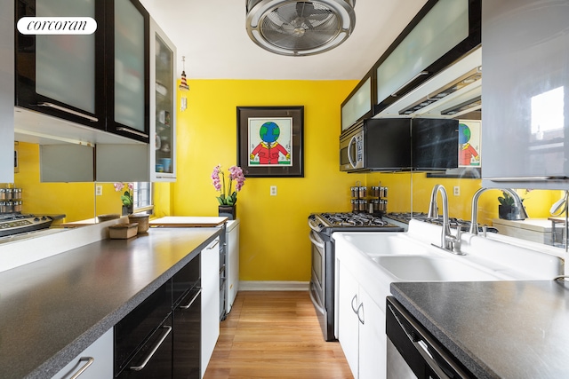 kitchen featuring dark countertops, light wood-style floors, appliances with stainless steel finishes, glass insert cabinets, and baseboards