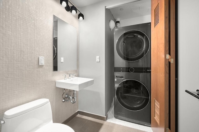 bathroom featuring tile patterned floors, stacked washer and dryer, sink, tile walls, and toilet