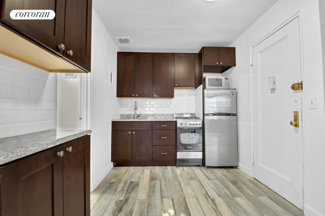 kitchen with appliances with stainless steel finishes, sink, decorative backsplash, light hardwood / wood-style floors, and light stone countertops