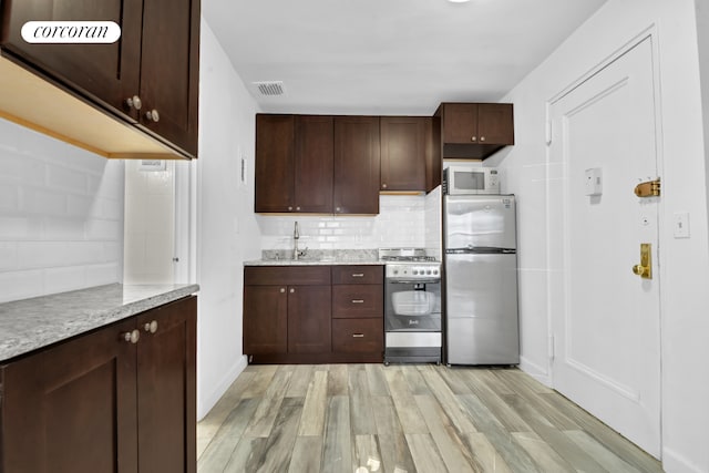 kitchen with appliances with stainless steel finishes, a sink, light wood-style floors, baseboards, and tasteful backsplash