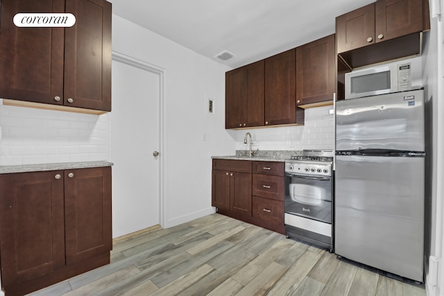 kitchen with appliances with stainless steel finishes, light wood-type flooring, decorative backsplash, and light stone counters