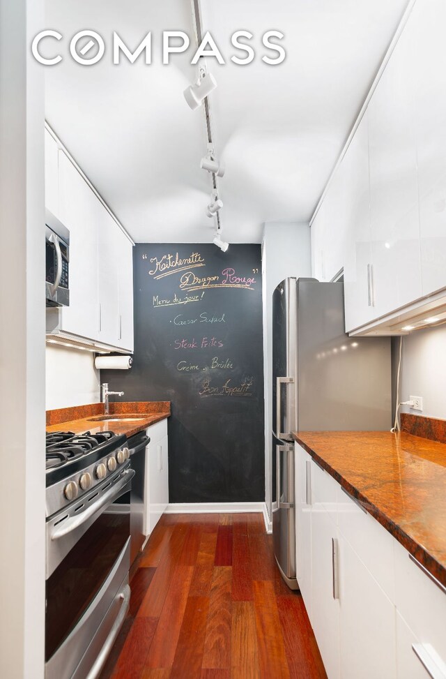 kitchen with white cabinetry, appliances with stainless steel finishes, dark wood-type flooring, track lighting, and sink