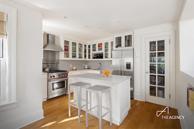 kitchen featuring light countertops, appliances with stainless steel finishes, a sink, a kitchen island, and wall chimney exhaust hood