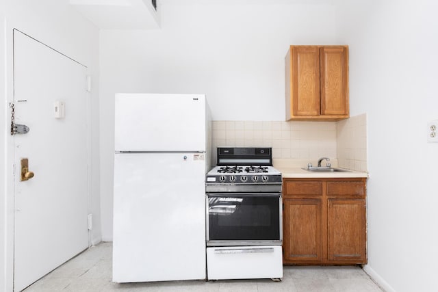 kitchen with tasteful backsplash, range with gas cooktop, freestanding refrigerator, light countertops, and a sink