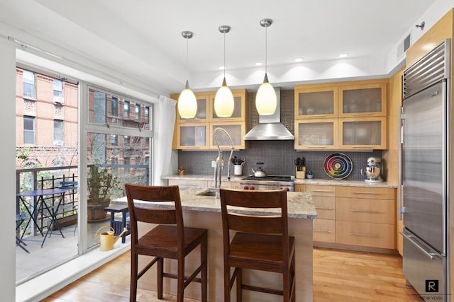 kitchen featuring light stone countertops, stainless steel built in fridge, glass insert cabinets, and pendant lighting