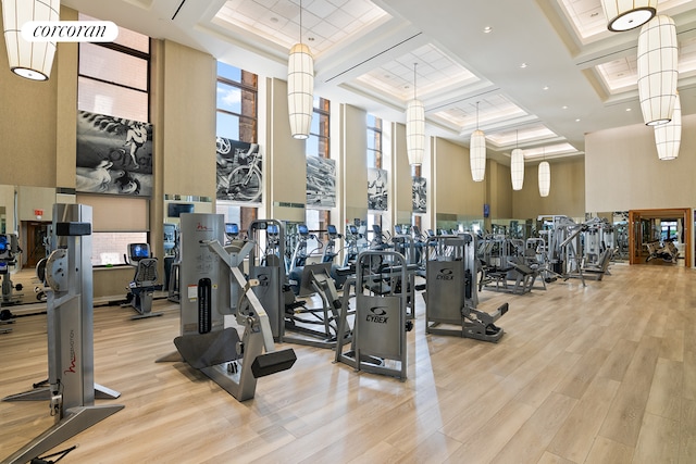 workout area featuring a high ceiling, wood finished floors, and coffered ceiling