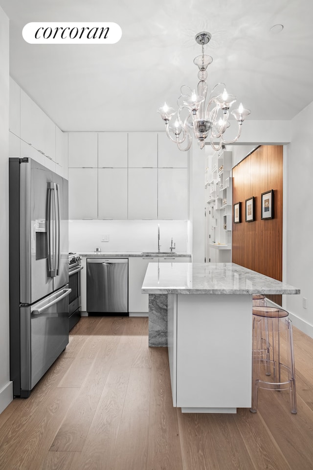 kitchen featuring modern cabinets, a sink, white cabinetry, light wood-style floors, and appliances with stainless steel finishes