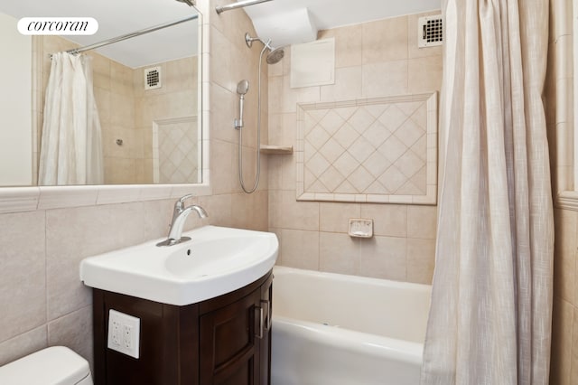 full bath featuring visible vents, toilet, shower / bath combo with shower curtain, vanity, and tile walls