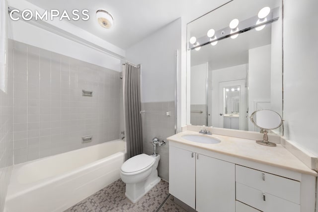 bathroom featuring tile walls, toilet, wainscoting, vanity, and shower / bathtub combination with curtain