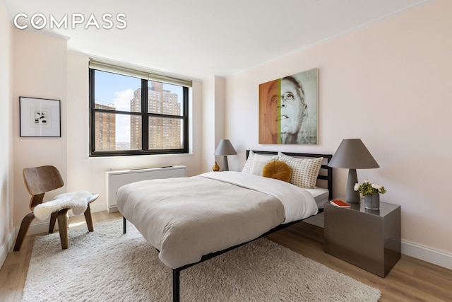 bedroom with radiator heating unit, baseboards, and wood finished floors