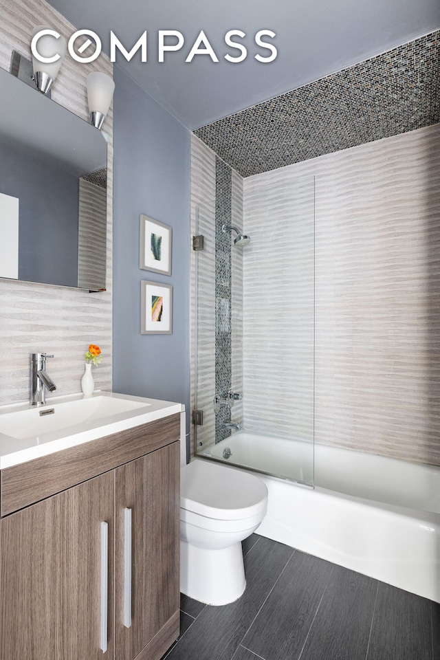 full bathroom with tasteful backsplash, wood finished floors, shower / bath combination with glass door, toilet, and vanity