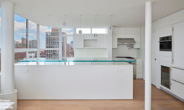 kitchen with oven, a view of city, ventilation hood, wine cooler, and light wood-style floors