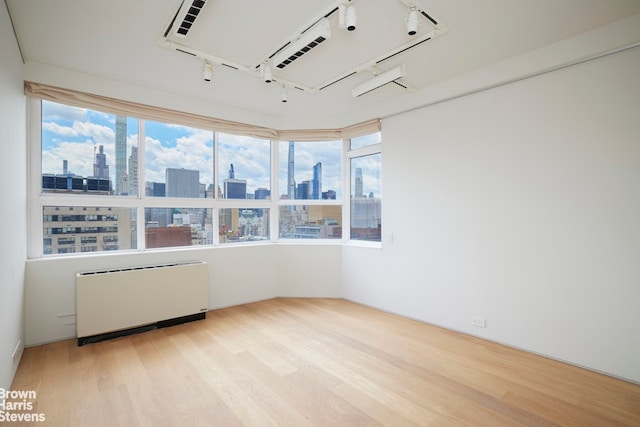 spare room with a view of city, radiator heating unit, wood finished floors, and a wealth of natural light