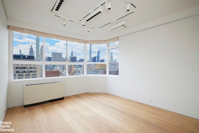 110 E 71st St Unit 19, New York City, NY 10021 - spare room featuring radiator, rail lighting, a view of skyline, wood finished floors, and healthy amount of natural light