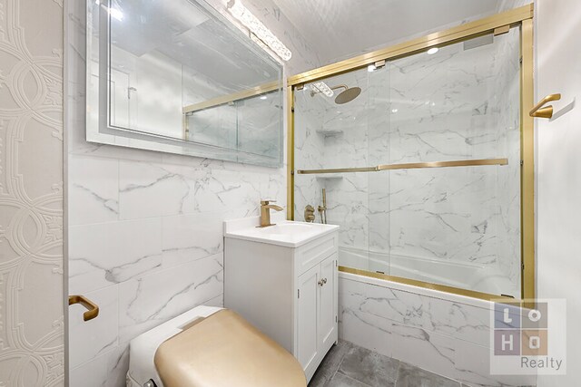 full bath featuring shower / bath combination with glass door, tile walls, and vanity