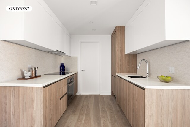 kitchen featuring sink, stainless steel oven, light wood-type flooring, white cabinets, and black electric cooktop