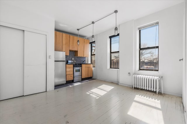 kitchen with radiator heating unit, modern cabinets, hanging light fixtures, stainless steel appliances, and backsplash