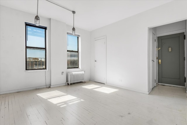 spare room featuring light wood finished floors, radiator heating unit, and baseboards