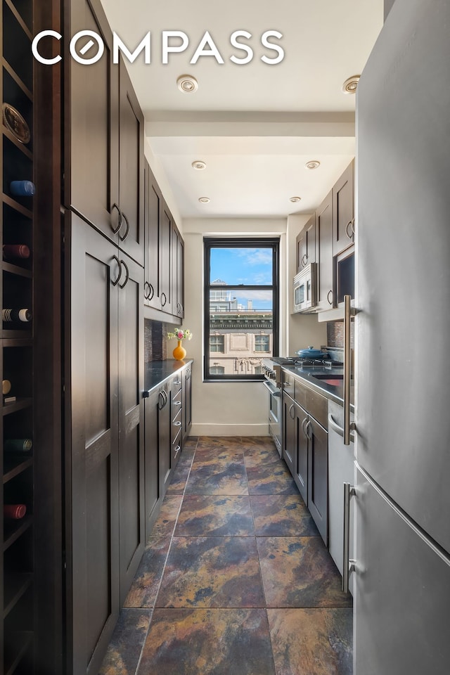 kitchen featuring dark countertops, baseboards, appliances with stainless steel finishes, and stone finish flooring